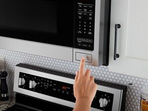 Hand pressing push button on over-the-range microwave.