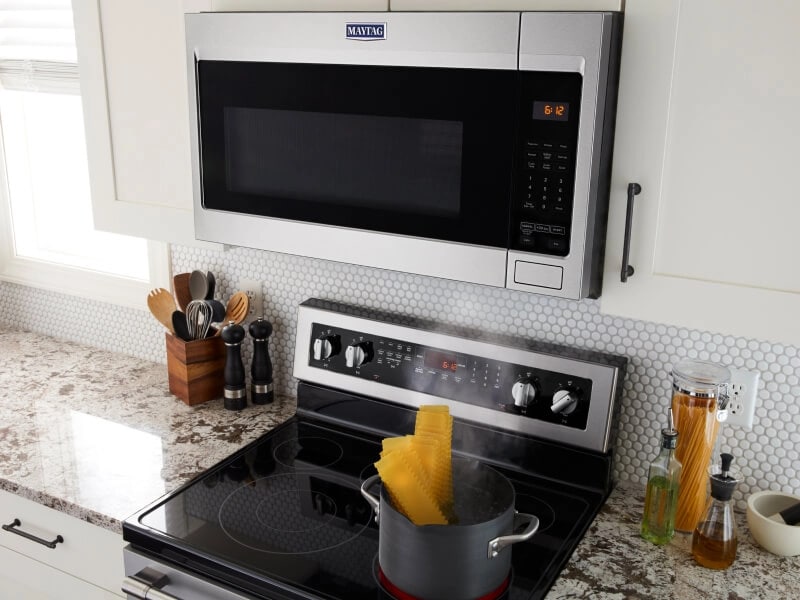 A Maytag® over-the-range microwave venting steam from a pot of pasta on a stovetop