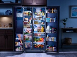 An open Maytag® refrigerator with an Arctic Blue Interior in a darkly lit kitchen