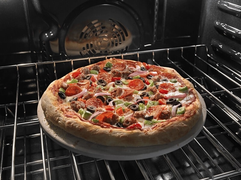 A supreme pizza baking on a pizza stone on an oven rack