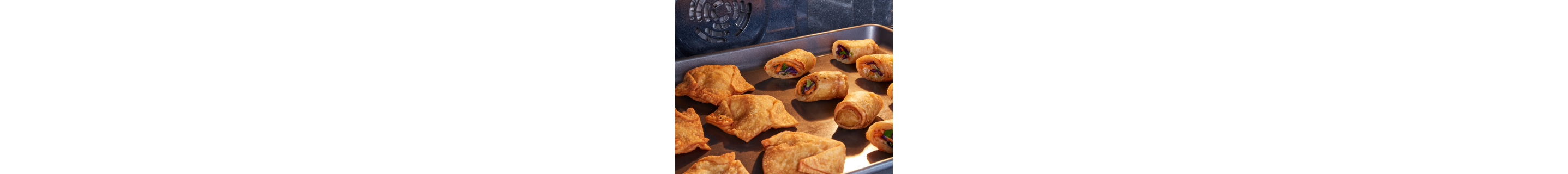 A pan of potstickers and egg rolls in an oven