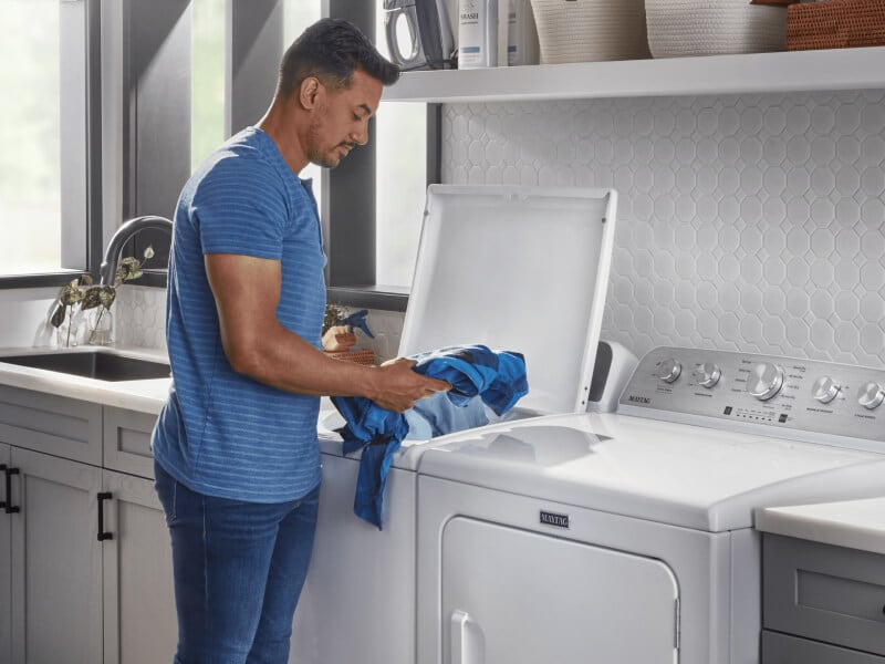 Person loading clothes into a white Maytagยฎ top load washer