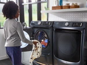 Person loading clothes into a Maytag® front load washer on a pedestal