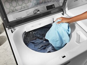Person placing clothes into a Maytag®  top load washing machine
