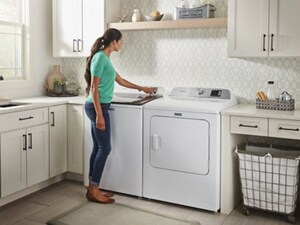 A woman operating a white, top load washer, next to a dryer in a laundry area