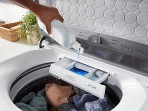 Hand pouring detergent over washer with colored clothes