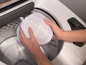 Hands holding mesh laundry bag over white washer