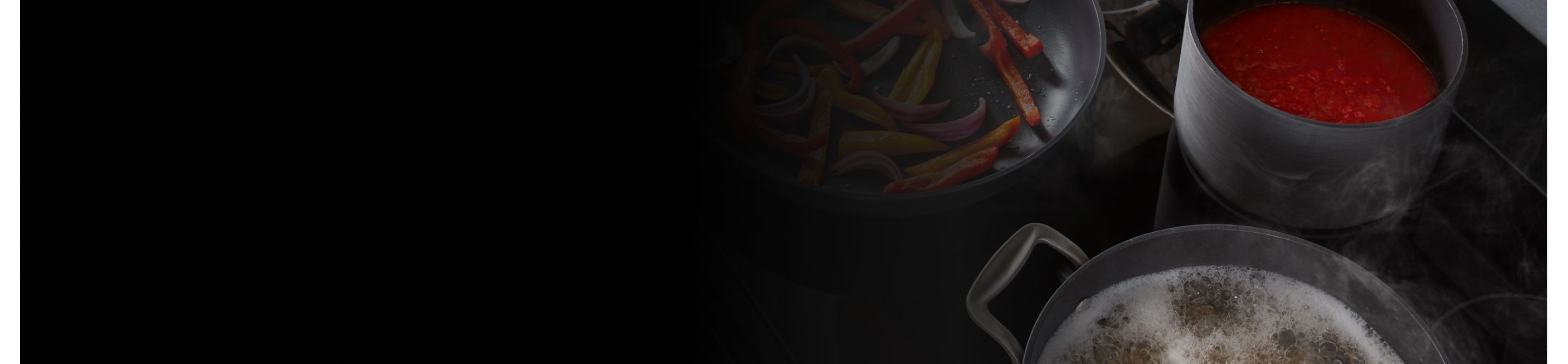Pots and pans full of food cooking on a KitchenAid® induction cooktop.