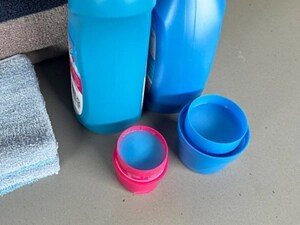 Two caps full of fabric softener next to bottles and towels