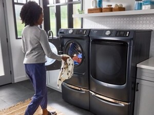 Person loading clothes into a gray, Maytag® front load washer on a pedestal