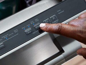 A finger operating the controls of a top control dishwasher
