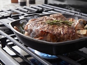 A close up of a frying pan with steak and potatoes cooking on a Maytag® gas cooktop