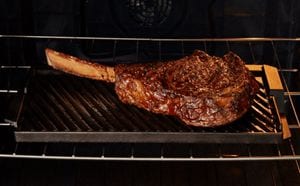 Large steak sizzling on the grill/griddle accessory in a Maytag® range