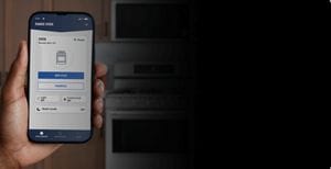 A hand holding a phone with the Maytag® Smart App open in front of a Maytag® range