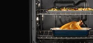 A chicken roasting in the oven with vegetables also roasting on top.
