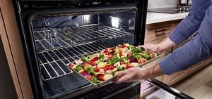 A person placing a tray of vegetables into the oven.