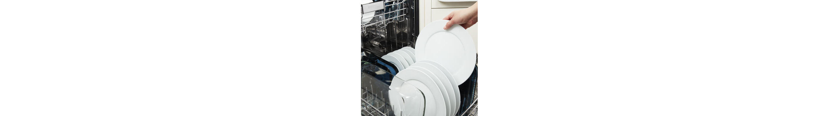 Person placing a white dinner plate in the bottom rack of a dishwasher